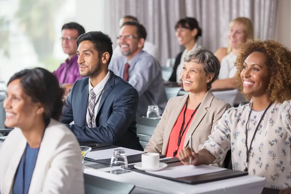 Business people seated in rows in a meeting room watching a financial presentation