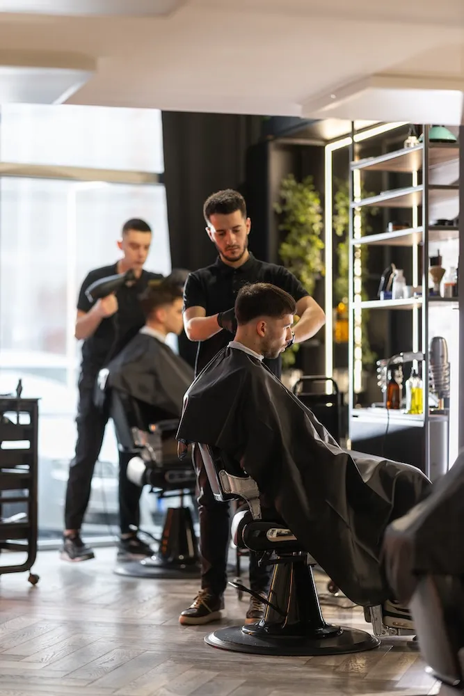 view of 2 hair stylists standing next to their respective patrons in a salon setting