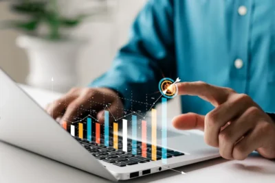 close-up shot of the side of a laptop and a person's hands pointing to a virtual bar graph overlayed onto the image