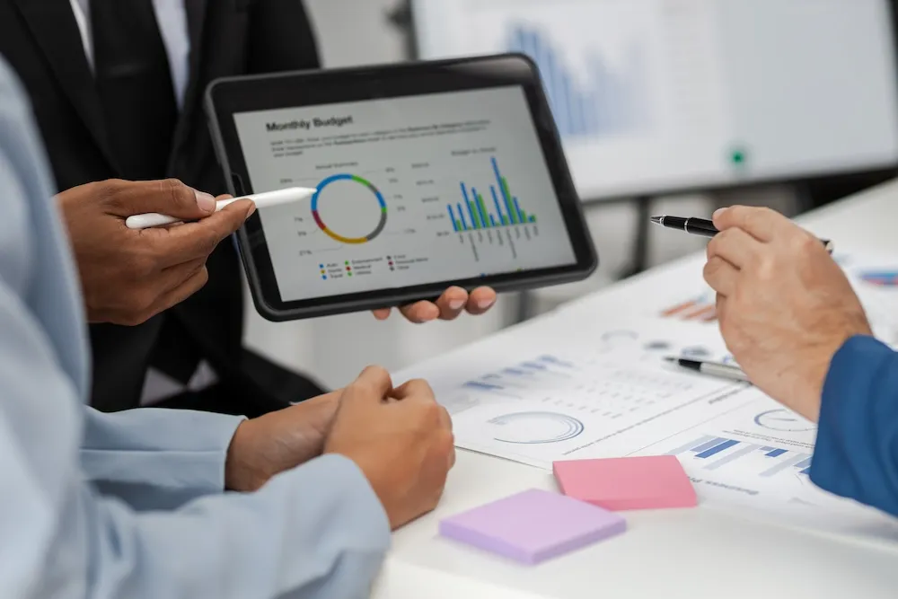 close-up shot of 2 hands from 2 different people pointing to colorful monthly budget figures on a tablet
